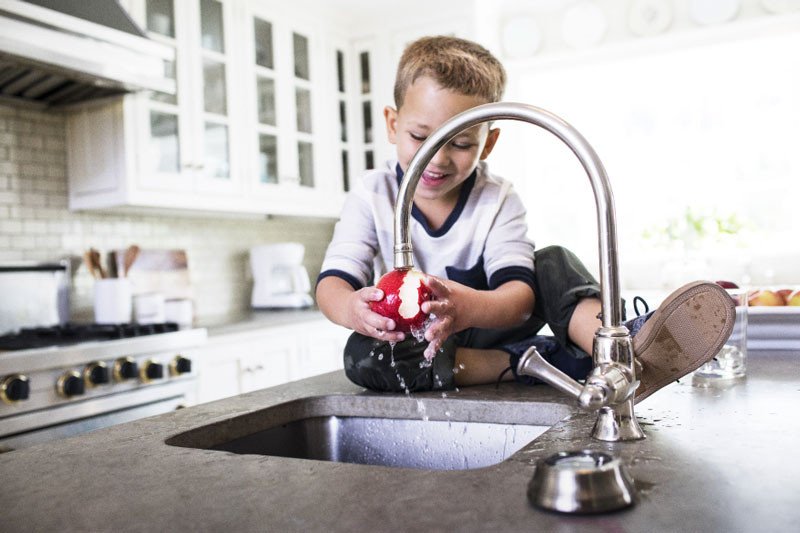 Boy washing fruit under faucet